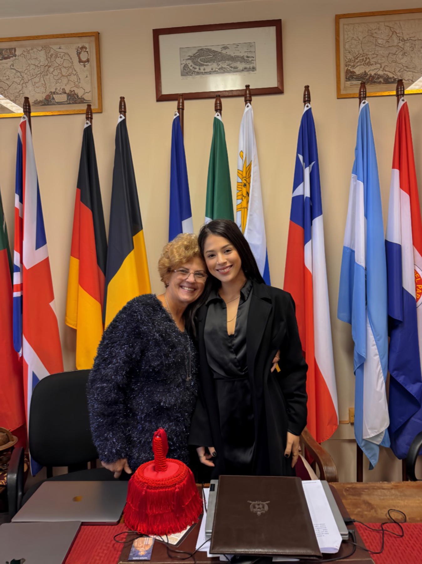 Ana Vanzin e Suzane Beatriz Vanzin juntas em uma sala com bandeiras